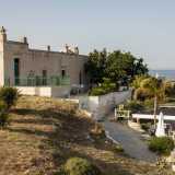 Sulla spiaggia di Porto Ghiacciolo, a Monopoli, tra bar e ombrelloni, si affaccia una masseria in pietra chiara e dalle linee squadrate, colorata da porte in legno azzurre e ringhiere in ferro dipinte di verde